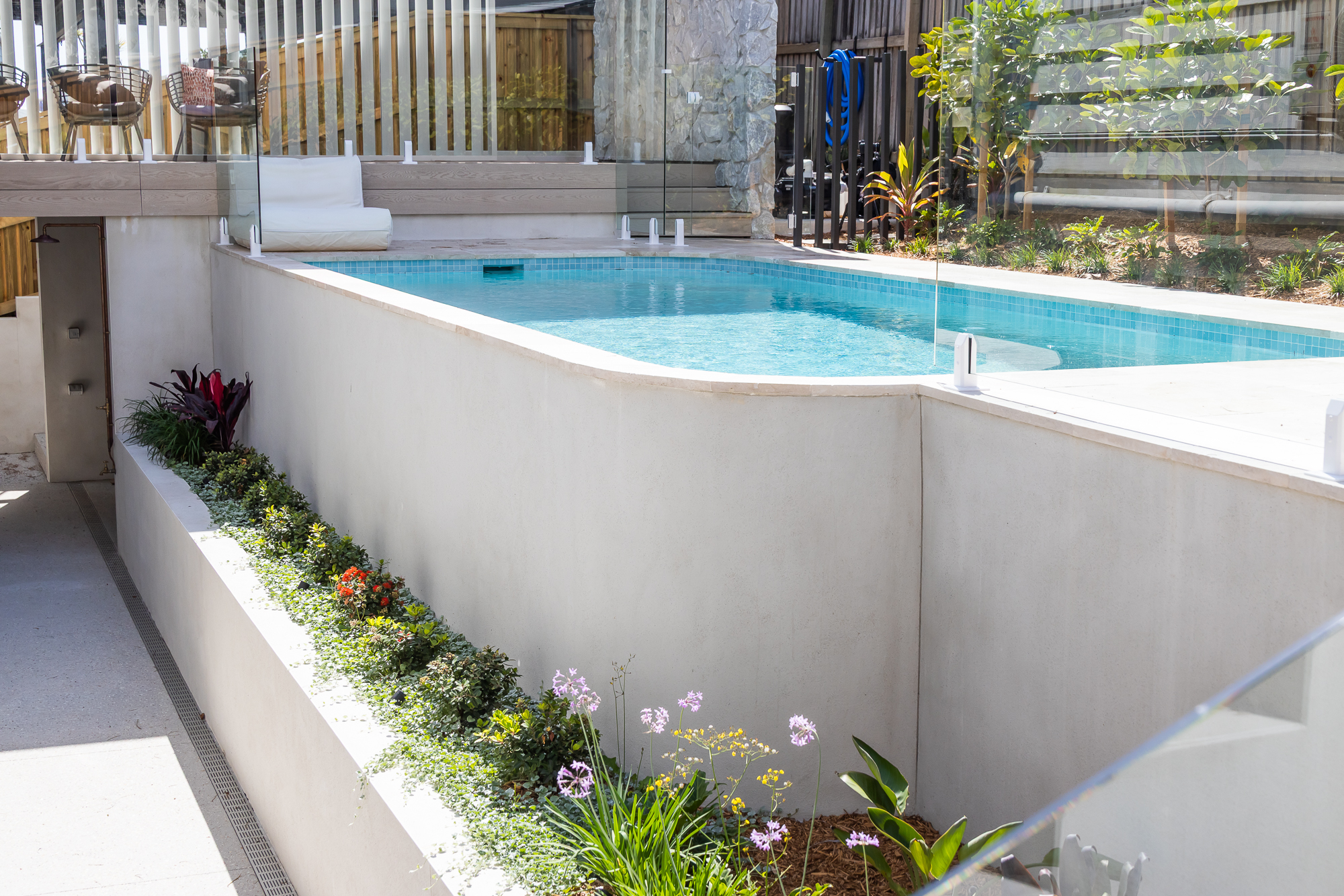 Pool with pale stone coping above a rendered planter, with a paved lower terrace and a slot drain along its edge