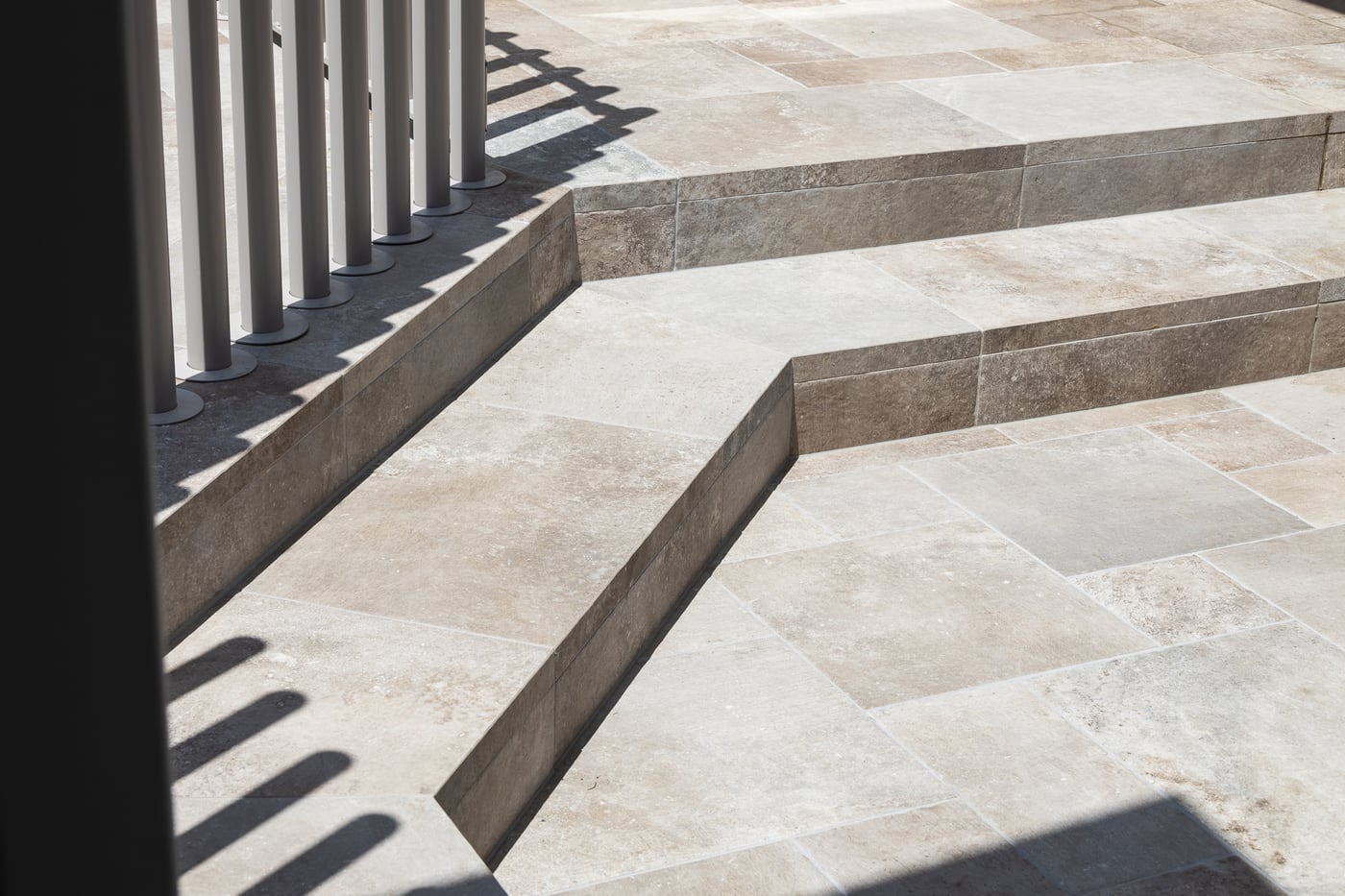 Pale stone paving stepping down in shallow terraces, with a slot drain running along the edge of the upper level