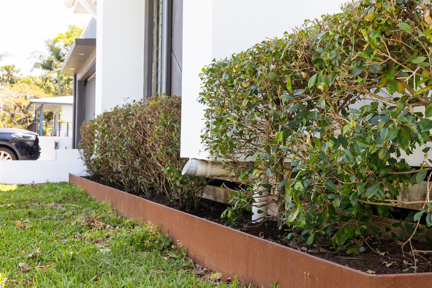 Downpipe discharging into a steel-edged garden bed beside a house and lawn